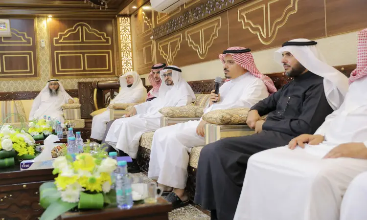 يجتمع عدد من الرجال مرتدين الغترة أو الشماغ والعقال بالإضافة إلى البشت السعودي، وهم يجلسون على أرائك فاخرة في قاعة مزينة خلال زيارة خادم الحرمين الشريفين. وقت واحد يحضر الميكروفون، بينما تتزين الطاولات أمامهم بتشكيلات من المشروبات والمشروبات.