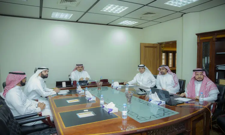 يجلس ستة رجال غترة سعودية، وشماغاً وقيلاً وبشتاً سعودياً حول طاولة الاجتماع في حين يغلب الطابع عليها الجاد. يتواصلون في جداول أجهزة الكمبيوتر المحمولة والوثائق وزجاجات المياه، فيما يتبادلون النقاش حول المسائل المتعلقة بالدراسات العليا. يوحي السياق أن اشتراك الاجتماع على نظام إدارة التعلم الإلكتروني مثل Blackboard، في إطار يعكس بوضوح استراتيجية جامعة القصيم الأكاديمية.