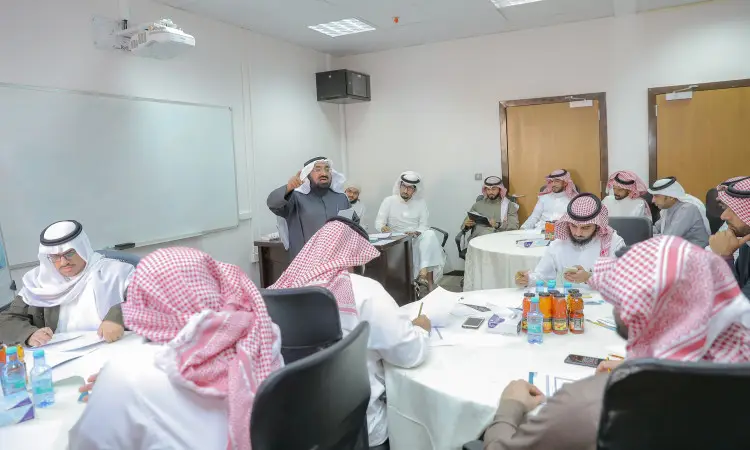 يجتمع عدد من الرجال الحاضرين الغترة أو الشماغ والعقال، ويضع المجموعة البشت السعودي، حول طاولات في إحدى قاعات كلية التربية في القصيم. تمت تسميتها من معلمي المنطقة، وقد جلسة اهتمام للاستماع إلى مكبر الصوت، ويلقي كلمته كجزء من البرنامج العلمي. تقترح على الجداول مشروبات وأوراق عمل تساهم في إثراء النقاش العلمي.