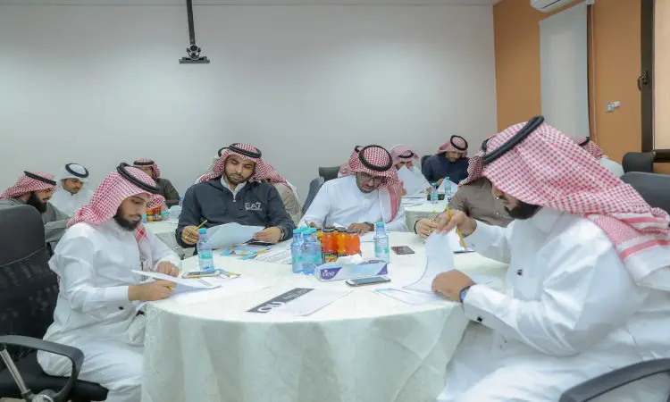 يجتمع عدد من الرجال مرتدين الغترة أو الشماغ السعودي مع القالب، ويرتدون البشت السعودي، حول الطاولات في القاعة يفضل ضمن البرنامج العلمي لكلية التربية في القصيم، حيث يتفاعل بمراجعة الطاولة وتدوين الملاحظات. هناك حاجة إلى الجداول المائية ووجبات المشاركين للمشاركين لعلمي المنطقة.