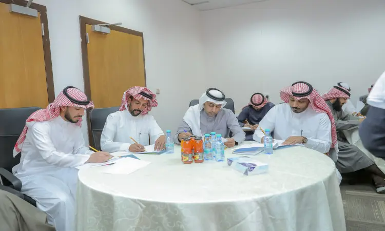 خمسة رجال يظهرون الغترة السعودية أو الشماغ والعقال، يضعون المجموعة البشت السعودي الرسمي، يجلسون حول طاولة طعام، مركزين على تدوين آراءهم خلال البرنامج العلمي في كلية التربية في القصيم. يناقش هذا المعلمو المنطقة أفكارهم في مكتب البيئة منظمة ومجهزة الحكمة والعصائر والمناديل، بما في ذلك الطابعة الرسمية لعدم التسجيل الأكاديمي.