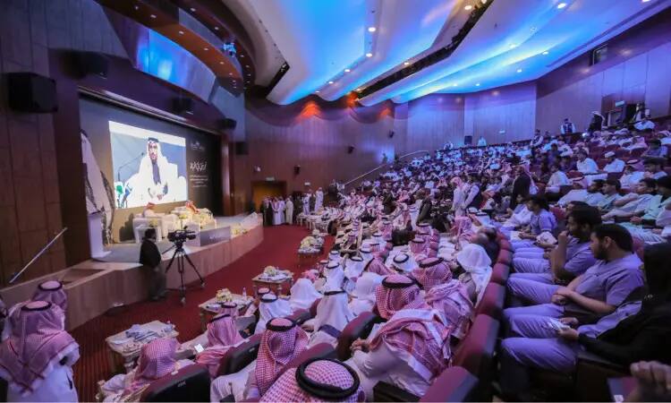 يحتفل بجمع غفير من الرجال، الحضور الغترة أو الشماغ والعقال والبشت السعودي التقليدي، في قاعة محاضرات في القسيم، ويستمعون باهتمام إلى المتحدث على المنصة أمام شاشة كبيرة خلال فعالية منصة الجامعة. ويجب أن يحضر البعض الزي الطبي (الاسكربز)، مما يشير إلى أن المقصود قد يتحمل طابعاً طبياً أو صحياً.