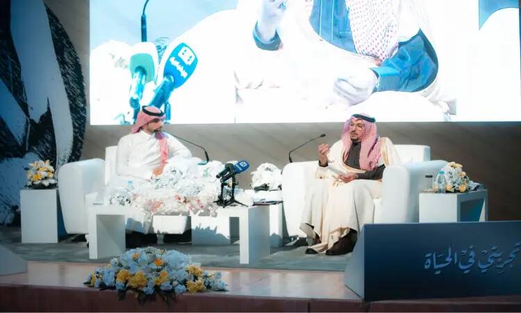 يجلس رجلان يرتديان الغترة أو الشماغ السعودي مع العقال والبشت السعودي على منصة الجامعة، يتبادلان تجاربهما في الحياة الرسمية. وتزيين الكراسي البيضاء وترتيبات زهور المسرح، في حين يتم وضع الميكروفونات بشكل كامل، حيث يحدد المكان الرئيسي على الشاشة الكبيرة في الخلفية.