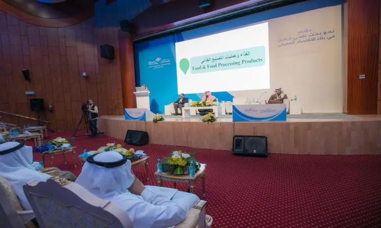 تُعقد جلسة نقاش علمي حول موضوع "الأغذية تنتج الطعام" على منصة خفيفة لعرض كبيرة ومنصة محاضرات، بحضور عدد من المشاركين الغترة أو الشماغ والعقال والبشت السعودي، حيث يتفاعل الحضور بطرح الأسئلة وإثراء النقاش العلمي في بيئة أكاديمية خاصة ضمن فعاليات جامعة القصيم.