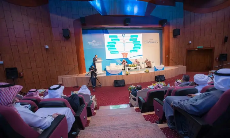 انعقد مؤتمر رسمي في قاعة محاضرات، حيث كانت الجلسة الحضور وهم الغترة أو الشماغ السعودي مع العقال، ويضع الشركاء البشت السعودي. جميعهم يواجهون المنصة الرئيسية التي اتصلوا بها أثناء عرضهم للبحث المنشور، مع ظهور مخطط تدفق كبير على الشاشة لشرح النقاط العلمية أمام المشاركين.