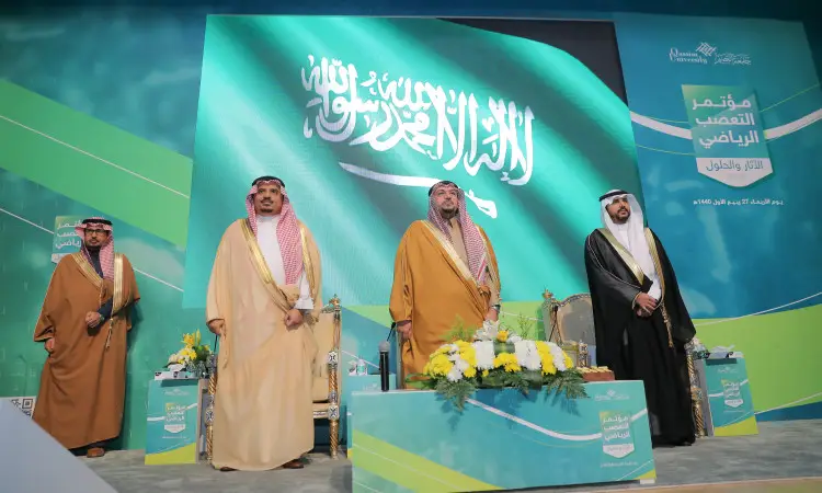 اتصال رجال مرتدين الغترة أو الشماغ والعقال، بالإضافة إلى البشت السعودي، على خشبة المسرح بجوار علم المملكة العربية السعودية، المنصة وزهور موضوعة الرائعة. وحضر في الخلفية شعار مؤتمر التعصب الرياضي ولافتة المؤتمر، بما في ذلك يبرز شريف سمو الأمير أمير منطقة القصيم لهذا الحدث الذي تحتضنه جامعة القصيم.