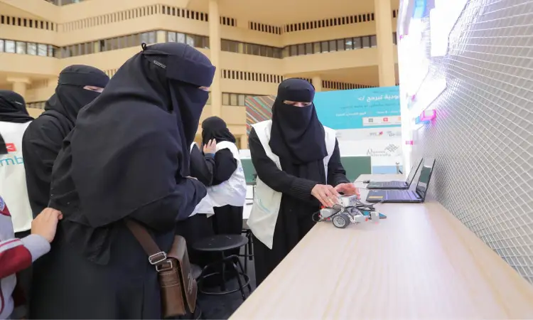 يتجمع عدد من، مرتديات العبوات السوداء والنقاب، حول أداة شراء روبوتية صغيرة آليًا من خلال فعالية التعلم أُقيمت في المدينة الجامعية في القصيم. إحدى جلسات استخدام الكمبيوتر المحمول، في مشهد يجسد روح المبادرة "السعودية لبرمجة" التقدم التقني في الجامعة. كما يتواجد بعض الحضور من الرجال بارتداء الغترة أو الشماغ مع العقال والبشت الرسمي السعودي، مما يؤكد الالتزام بالهوية السعودية الأصيلة داخل رحاب جامعة القصيم.