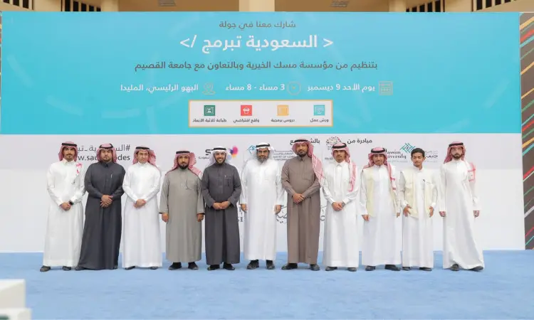 القطة مجموعة من الرجال مرتدين الغترة أو الشماغ والعقال مع البشت السعودي على خشبة المسرح أمام خلفية زرقاء تحمل نصوصًا وشعارات باللغة العربية. ويعكس هذا المشهد مشاركة جامعة القصيم في فعالية "السعودية ت ت" الاجتماعية بالبرمجة، والمنظمة بالتعاون مع الجامعة.
