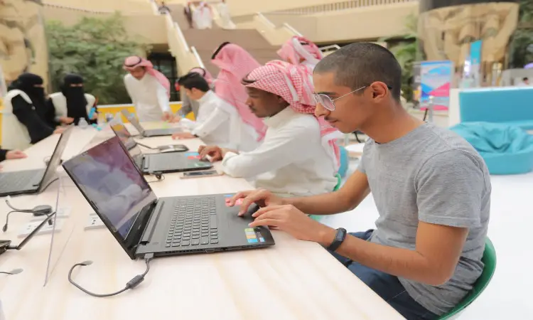 يجتمع مجموعة من الناس في المدينة الجامعية خلال فعالية "السعودية تبرمج"، حيث تجتمع المجموعة الغترة السعودية أو الشماغ مع العقال والبشت السعودي، في حين يجتمع العديد من الملابس. وبعد ذلك كله على أجهزة الكمبيوتر المحمولة حول طاولة طويلة ضمن مساحة داخلية حديثة.