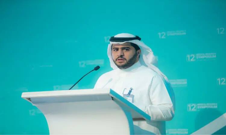 وقف مدير الجامعة مرتدياً غترة سعودية مع عقال وبشت سعودي رسمي خلف منصة الخطابة، مكبراً أمام خلفية الفن الفيروز تتوسطها عبارة "الملتقى الطبي البحثي الثاني عشر" منظم الأبيض. مدير الجامعة متفاعلاً وهو يمسك الميكروفون من خلال كلمته الرسمية للهدف.