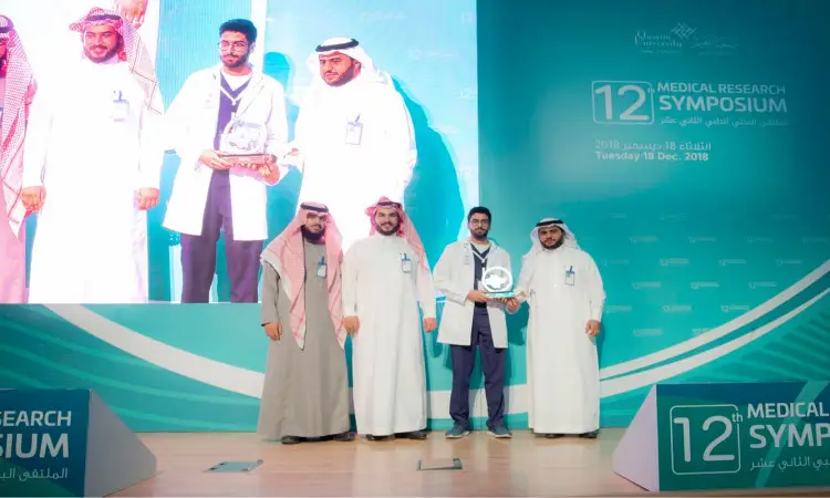 أربعة رجال تألقوا بالغتة أو الشماغ والعقال، مع البشت السعودي والعاطفي الطبي على خشبة المسرح في الملتقى البحثي لجامعة القصيم، حيث نجح أحدهم في الحصول على جائزة بيده. وتعرضت الشاشة الكبيرة خلفهم لصورهم بشكل واضح، كما تسلط الضوء على الفيروسات الجديدة التي تم تقديمها من قبل اللجنة العلمية خلال الفعالية.