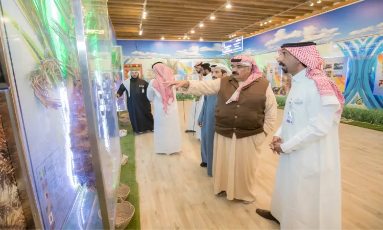 يجتمع مجموعة من الرجال مرتدين الغترة أو الشماغ السعودي مع العقال والبشت السعودي، لمتابعة ومناقشة العروض الزراعية في أحد أجنحة المعرض المقام ضمن فعاليات الجنادرية، حيث تتضمن الأجنحة معلوماتية عن الأهمية الغذائية، وتبرز الزينة الملونة في المكان الطابع التراثي للفعالية.