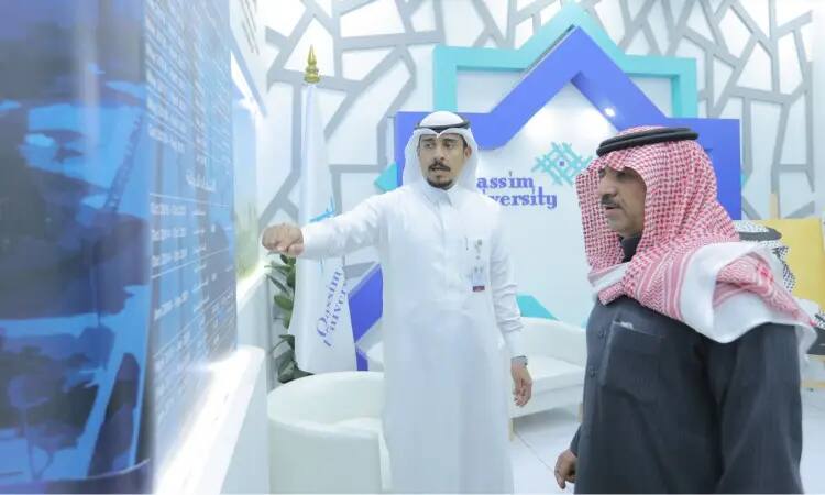 رجلان بزي سعودي رسمي داخل إحدى قاعات جامعة القصيم، حيث يرتدي كل منهم غترة أو شماغاً وطنياً مع عقال، ويكمل مظهره السعودي التقليدي بالبشت. يشير أحد الرجالين إلى لوحة عرض المعلومات بينما يتابع الآخر باهتمامه. مواكبة التطورات العصرية في الجدران، بالإضافة إلى شعار الجامعة، مع إبراز إشارات لمناسبتي "الجنادرية 33" و"مسيرة وإنجاز".