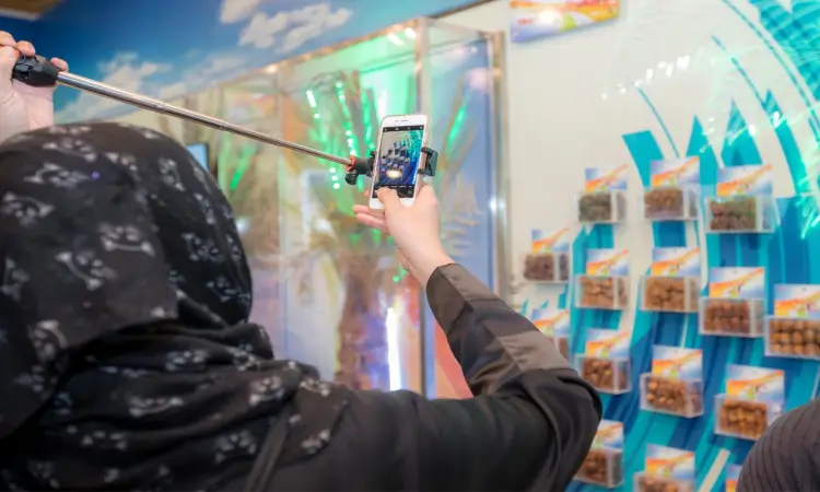 شخص يرتدي غترة سعودية من جاكوزية ويضع عقالاً أنيقاً، يستخدم عصا التصوير الذاتي، وصورة أمام جدار العرض والتعاون العمالي الصغير، يُحتمل أن تكون منتجات تمارس من علامة "النخلة"، وذلك ضمن فعالية لمهرجان الخيال الجنادرية، حيث يسلط الضوء على المكان مقابل زاهية. اكتمل سجل السعودية التراثية بارتداءه البشت السعودي الرسمي المعبر عن الهوية الوطنية.