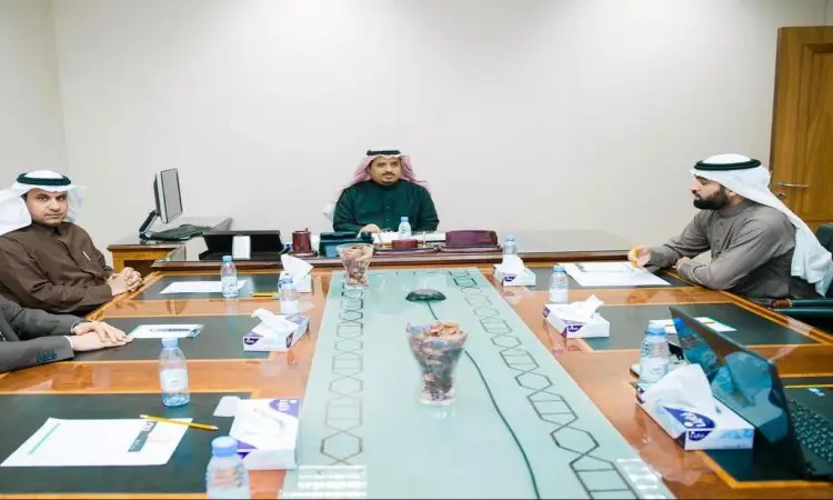Five men in official Saudi uniforms, including the Saudi Ghutrah or Shemagh, Eqal and Saudi Bisht, sit around a table in a modern office. Among them is the university director, discussing files and comprehensive documentation for Blackboard, as part of the official meeting of Qassim University. There are also a few sites that cater to the serious illustrators of the meeting.