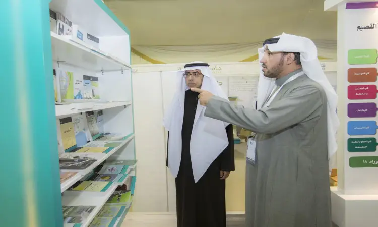 رجل يرتديان غترة أو شماغًا سعوديًا مع عقال وبشت سعودي داخل جناح في معرض القصيم للكتاب، يتأملان في محتويات مكتبة الخصوصية كتبًا وكتيبات مُقترح على الرفوف. يشير إلى ذلك المصطلح، بينما يستمر في تحديد اللوحات اليمنى.