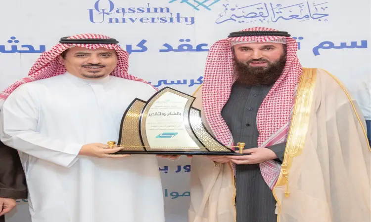 يرتدي رجلان الغترة أو الشماغ والعقال بالإضافة إلى البشت السعودي، مع مرور الوقتان معاً درعاً تكريمياً خلال إحدى الفعاليات الرسمية. تذكير في التذكير بشعار الشيخ علي بن عبدالرحمن القرعاوي لعلوم القرآن الكريم. يبتسم ويواجهان عدسة الكاميرا.