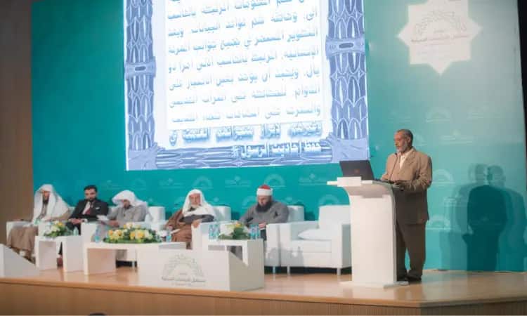 قام رجل بكتابته على المنصة في المؤتمر الدراساتي الحديث، بينما جلست خلفه خمسة أشخاص لازم الغترة أو الشماغ السعودي مع العقال والبشت السعودي، في ضوء الطبعة الرسمية للمناسبة. وظهرت خلفهم شاشة كبيرة تحمل نصوصاً باللغة العربية حول السنة النبوية التعليمية العلمية، مما أبرز المهنية والرسمية لجامعة القصيم.