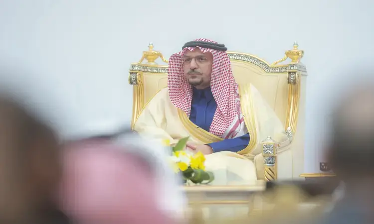 يرتدي رجل الزي السعودي الرسمي، متمثلاً في الغترة أو الشماغ السعودي والعقال، بالإضافة إلى البشت السعودي والنظارات، على كرسي ذهبي فاخر خلال المؤتمرات الدولية. تتوسطه طاولة مزينة بأزهار جديدة، وتتقدم في الصورة بعض الشخصيات الجامعية بشكل غير واضح.