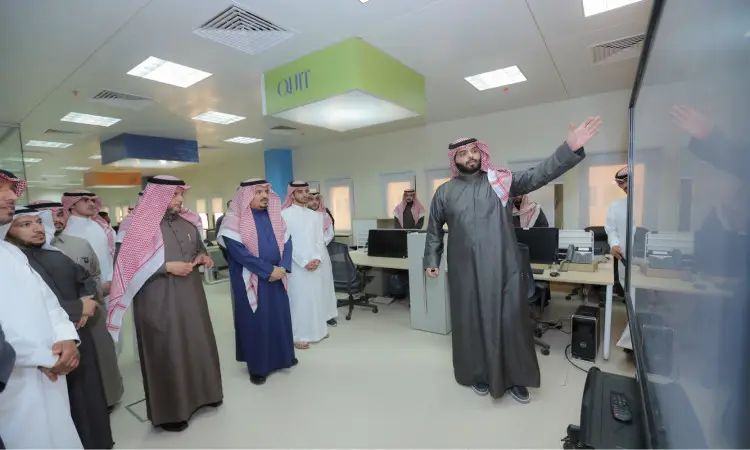 يجتمع مجموعة من الرجال الحاضرين الغترة أو الشماغ السعودي مع العقال والبشت السعودي في أحد الطلاب في قاعة القصيم الحديثة، حيث يستمعون باهتمام إلى أحد الحضور وهو يشير إلى شاشة كبيرة ويشرح موضوع الأمن الإلكتروني، وذلك عبر بيئة عمل مجهزة بأجهزة الحاسب الآلي ومحطات العمل.