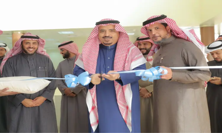 مجموعة من الرجال الحاضرين الغترة أو الشماغ والعقال مع البشت السعودي، يبتسمون خلال مراسم افتتاح الخدمات الإلكترونية في جامعة القصيم، حيث يقوم أحد بقص شريط أزرق إيثانًا بانطلاق خاص، فيما يحضر هذا الحدث ويشاركون في الاحتفال به.
