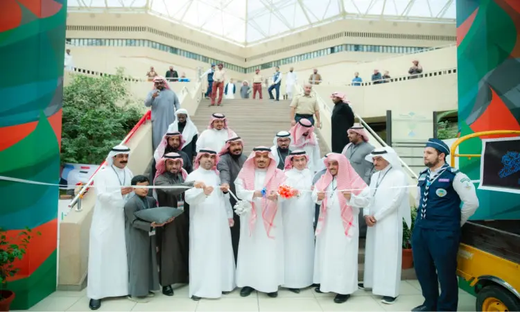 بحضور مدير جامعة القصيم وعدد من أربعة، قام مجموعة من الرجال مرتدين الغترة والشماع والعقال والبشت السعودي بقص الشريط إيذانًا بافتتاح مهرجان تراث الشعوب، وذلك في قاعة مغلقة. وذهبت في خلفية الصورة بعض الحاضرين يتابعون الحدث من على الدرج، بينما اتصلت كشاف بزيه الرسمي في الجهة اليمنى من الصورة.