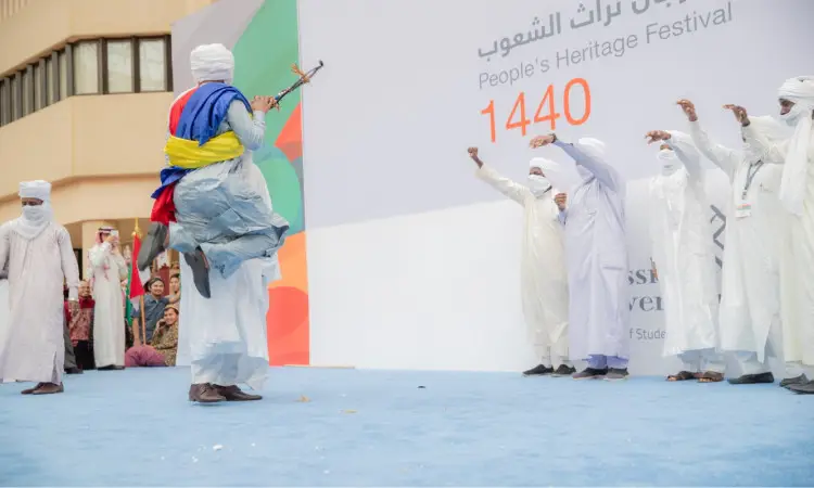 مجموعة من الرجال يرتدون الثياب البيضاء التقليدية، ويضعون الشماغ والعقال، وبعضهم يرتدي البشت السعودي، يؤدون عرضاً مميزاً على تيست الخارجي خلال فعاليات مهرجان تراث الشعوب 1440 في القصيم. ويبرز أحد المشاركين وهو يقفز ممسكاً بصا، بينما يقوم بحركات ملتزمة بالتكامل مع العرس التشادي الأصيل.