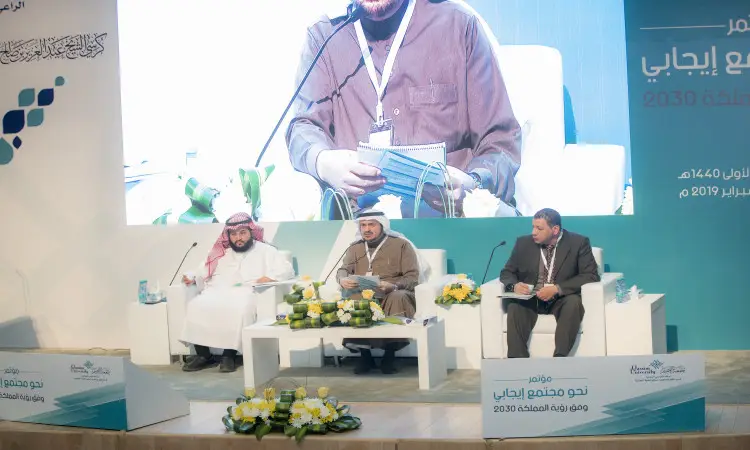 يجلس ثلاثة رجال على المنصة وهم ينتظرون الغترة السعودية أو الشماغ مع العقال والبشت السعودي، ويتحاورون أيديهم الميكروفونات والأوراق خلال الجلسات العلمية ضمن فعاليات مؤتمر رؤية 2030 في جامعة القصيم. يؤخذ خلفهم شبكة الاتصال الرئيسية صورة رئيسية، بينما تعتبر الزينة باللون الازرق والأبيض وتنسيقات الزهور علمية تبرز قيم المجتمع.