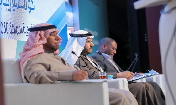 يجلس ثلاثة رجال على منصة النقاش، وهم تولى الزي السعودي التقليدي في الغترة أو الشماغ السعودي مع العقال والبشت الرسمي السعودي. أمام كل منهم أوراق وأكواب الشاي. الحد من صحتهم وتحمل نصوصا عربية تشير إلى الفعالية ضمن مؤتمر رؤية الأطفال 2030، وتركز اللافتة على الجلسات العلمية وتعزز مفهوم المجتمع القيادي، وذلك في إطار التنظيم الرسمي في القصيم.
