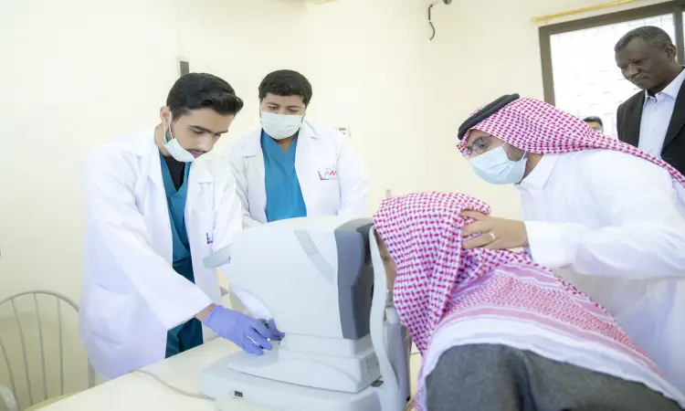 يقوم طبيبان بمساعدة رجل مسن يرتدي الغترة والعقال والكمامة أثناء خضوعه لفحص البصر باستخدام جهاز الملفات الطبية للعيون، وذلك في دار رعاية الشركاء بمحافظة عنيزة، حيث يراقب الرجل آخر ارتدى الشماغ والبشت السعودي للاستراحة من العصور الحديثة في البناء، وما إلى ذلك في إطار جهود جامعة القصيم لدعم الخدمات الصحية للمسنين.