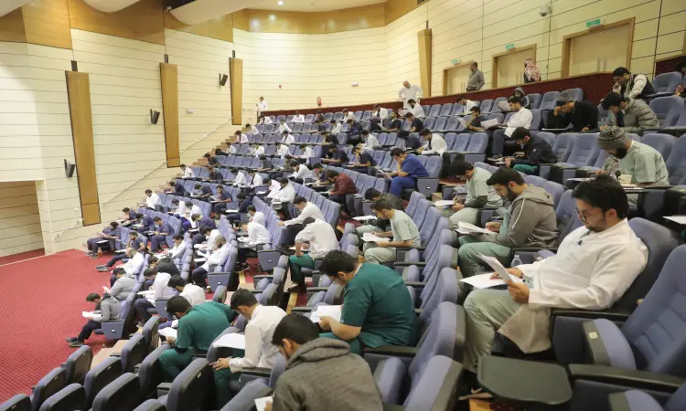 ينتظرون، تومضٌ منهم الزي الطبي الرسمي من كليات الطب المختلفة في جميع أنحاء المملكة، في قاعة محاضرات ومضيئة ضمن جامعة القصيم. تتباعد النساء بشكل خاص بين النساء اللاتي يحرصن على الاهتمام بأوراق الثقب أو أجهزة الكمبيوتر المحمولة أثناء تجاويف المقاييس. ولاحظ حضور بعض الطلاب بارتداء الغترة السعودية أو الشماغ والعقال، في حين اكتمل ظهور الفرق الآخر بالشت السعودي، في مشهد عكسي رسمي والهوية الوطنية في هذا المتدرب الأكاديمي الراقي.