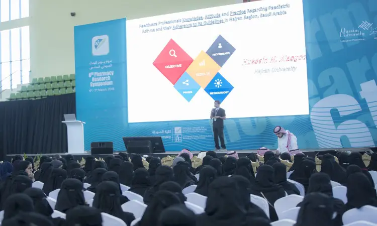 A man dressed in a Saudi Arabian ghutra, aqal and bisht gave a highly scrutinized presentation to a crowd of women wearing black hijabs as part of the Pharmacist Search event at Al-Qassim University. Flowing diagrams are used to identify means of distribution in the health sector.