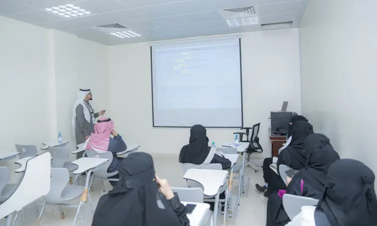 اتصل أحد أعضاء هيئة التدريس مرتديًا غترة سعودية وقالًا وبشتاء سعوديًا أخيرًا في قاعة حماية محاضرات كلية الطب في القصيم، مشيرًا نحو عرض الشاشة بشكل عرضي، بينما يجلس عدد كبير من الطلاب والطالبات، يرتدي معظم الطلاب عباءات ونقاب، منصتين باهتمام أثناء دورة العملاق.