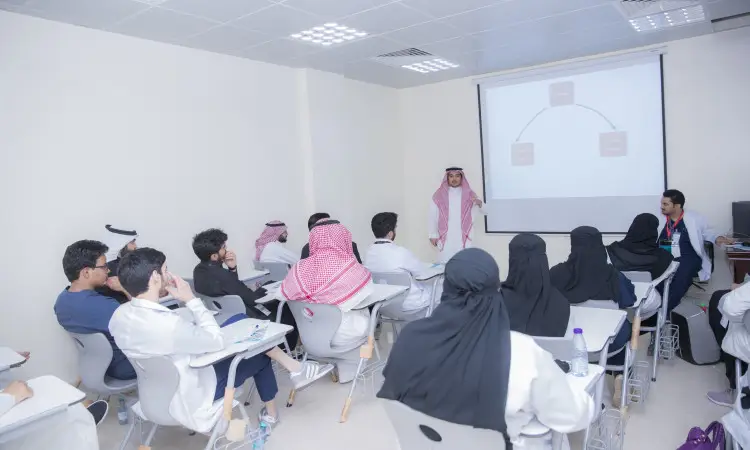 جلسة في كلية الطب في جامعة القصيم لثلاثينيات الجلوس على اليمين؛ إذ ارتدت الطالبة الشماغ السعودي مع العقال والبشت السعودي، حيث ترتدي الطالبات الآداب التقليدية. يستمتع الجميع باهتمام بالمحاضر الذي يقدم عرضًا لمخطط أعلىي مُسقط على السبورة أثناء دورة العملاق.