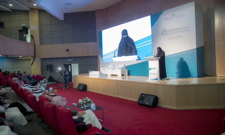 ألقت ترتدي ملابس بيضاء ونقابًا، حتى حضورها الرسمي وهي سيدة فلوريدا خلف المنصة خلال الملتقى البحثي الحديث الخاص بالتأهيل الطبي، وذلك في القاعة لمؤتمرات جامعة القصيم. وخلف مقاعدها شاشة كبيرة تعرض المحتوى، أثناء حضورهم ـ من أعضاء هيئة التدريس والضيوف ـ في ريد ريد فورون تيراس، حيث غطت بين الحضور عدد من الرجال مرتدين الغترة أو الشماغ مع العقال والبشت السعودي في سبتمبر عكس الطابعة الرسمية للملتقى ومكانته العلمية المتقدمة.