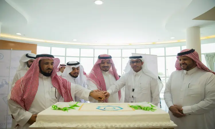 يجتمع عدد من رجال مرتدين الزي السعودي الرسمي الواسع في الشماغ والعقال والبشت السعودي حول قالب كعك الفروسية الكبيرة خلال فعاليات ملتقى القصيم لطب الأسنان، حيث يقوم ثلاثة منهم عمليهم معاً للمساعدة لقص الكعكة. ويظهر الجميع مبتسمين بصفتها القوية برئاسة مدير الجامعة.