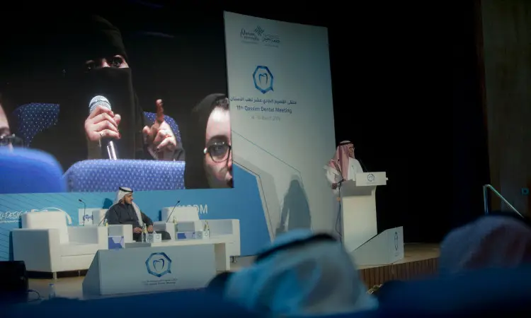 يلقي أحد المقصودين كلمة أمام الحضور في مؤتمر ملتقى طب الأسنان في القصيم، حيث خلفه على الشاشة الكبيرة تلفزيون مباشر لامرأة من فوق ترتدي عباءة وبشت سعودي وتتمسك بالميكروفون، وتناقش أحدث التوجهات في علاج وزراعة الأسنان. الاتصال بها أحد الحضور مرتدياً شماغاً سعودياً مع عقال، ضمن احترامها للمجتمع المبدعين المبدعين.