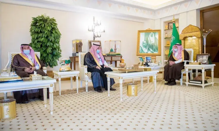 يرتدون ثلاثة رجال بلباس سعودي تقليدي في قاعة فاخرة تزينها لمسات ذهبية، حيث يرتدون كل منهم غترة أو شماغاً وقالاً إضافة إلى البشت السعودي مع التزامهم بارتداء الكمامات الطبية. وتبرز خلفهم راية المملكة العربية السعودية، ورئيسة مؤطرة، ونبتة كبيرة ضمن احترام احترام الفنان الرسمي للقاء مع القصيم في منطقة القصيم.