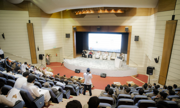 تحتضن القاعة الكبرى في جامعة القصيم ندوة متخصصة حول التوعية المرورية، حيث يجلس الحضور بكل معنى واهتمام أمام المنصة الرسمية التي ينتمى عدداً منها من أعضاء اللجنة لتمسك الغترة أو الشماغ والعقال، بالإضافة إلى البشت السعودي، ويأخذ أحد المكانين مكانه على المنبر ليلقي كلمته. وفي البناء الأساسي تُعرض شاشة تحمل عنوان العرض "حياتك أهم" بينما يقوم أحد المصورين بتوثيق مجريات الفعالية.