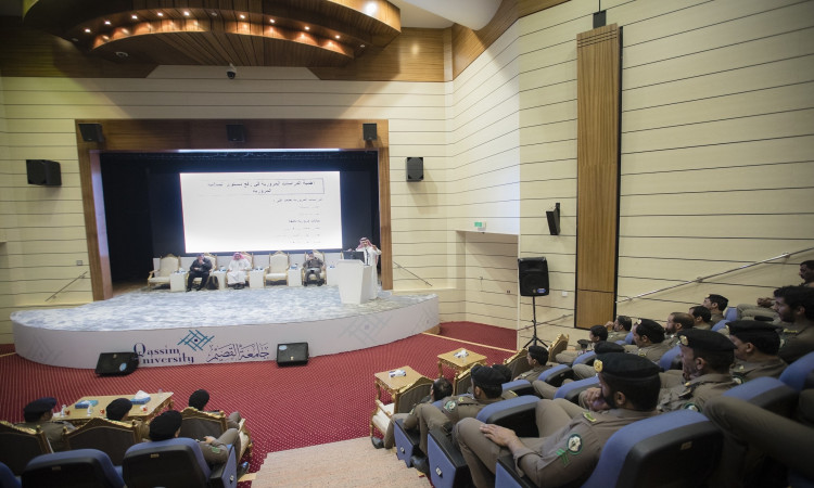 الأمر مرتديًا غترة وعقال وبشت سعودي عند المنصة في القاعة محاضرات حديثة في القصيم، مع كلمته خلال ندوة الجامعة حول التوعية المرورية، موجّهًا خطابه إلى الحضور من رجال الأمن بزيّهم الرسمي. مكوناته منصة شاشة العرض الكبيرة تحمل شعار "حملة حياتك اليومية".
