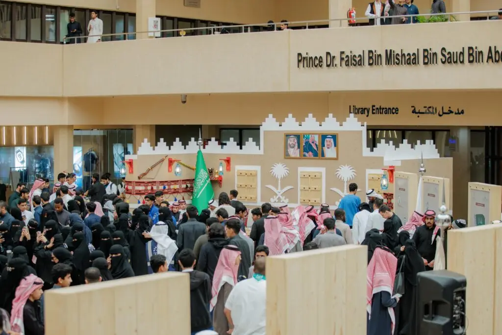 جمعٌ كبير في جميع الفعاليات المقامة داخل الجامعة، بالقرب من منصة يُزيّنها علم المملكة العربية السعودية وتتحمل شعار فعاليات الجامعة. ارتدى العديد من الحضور الزي الوطني الرسمي، حيث ظهر رجال بلباس الغترة أو الشماغ السعودي مع العقال والبشت السعودي. وبرزت لافتة باللغتين العربية والإنجليزية تنبه إلى الإدخال الحكومي فاءً بيوم التأسيس المجيد.
