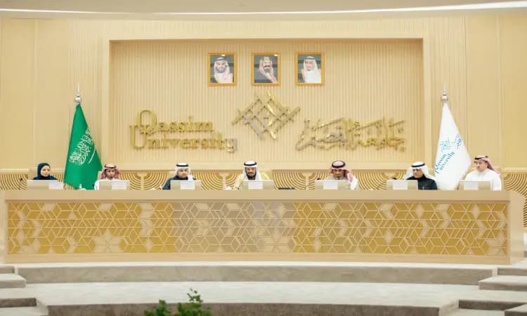 Seven members gather at a long podium in Al-Qassim Hall, with the Saudi Ghutra or Shemagh, Eqal and Bisht behind them and university flags lining the wall, during the 37th meeting of the deans of dental colleges.