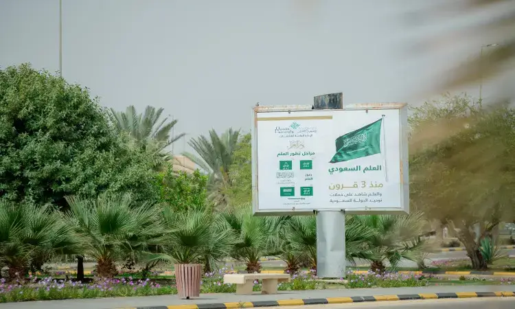 في مشهد رسمي يتتبع في القصيم، يبرز لوحة إعلانية وسط منطقة منسقة باربعة نباتات وأشجار النخيل، وتتعرض لوحة علم المملكة العربية السعودية مع عبارات عربية تحت بيوم العلم. ويقف بجانب اللوحة عدد من الرجال الثمانية الثوب السعودي مطرزًا بأناقة البشت السعودي، ويضعون على رؤوسهم الشماغ أو الغترة والعقال في صورة تجسد الأصالة الوطنية. اكتملت بوجود خطوط العنقني المعترف بها بالتخفيض والسوداء.