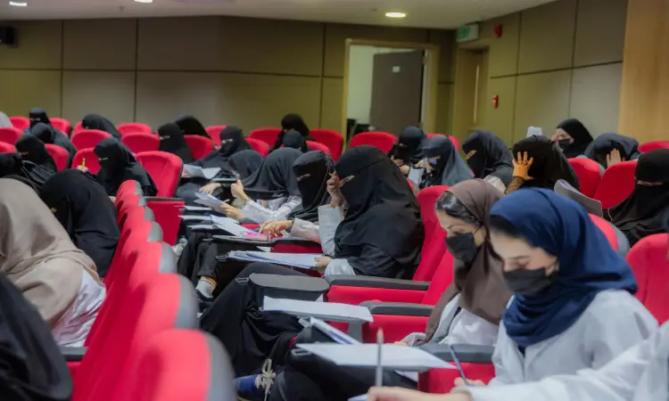 A group of women wearing a Saudi Ghutra or Shemagh with a Saudi Eqal and Besht, sit in the red vests listed at Qassim University, writing or jotting down notes on specialized boards, during a biometric test.