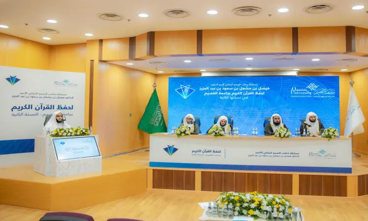 يجلس أربعة رجال تحت الغترة أو الشماغ السعودي مع العقال والبشت السعودي على منصة المؤتمر في المسرح، وذلك ضمن فعاليات مسابقة الأمير فيصل بن مشعل حفظ القرآن الكريم، وأمامهم وتزيينات من الزهور. ويجلس رئيس الجامعة على منصة ماكياج، لتوفير أعلام المملكة العربية السعودية والجامعة بشكل واضح في المشهد.