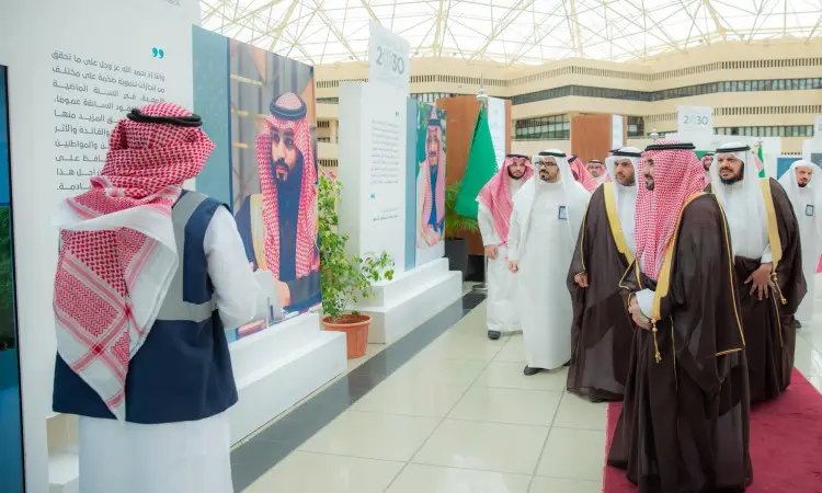 يجتمع مجموعة من الرجال بزيهم السعودي الرسمي، مرتدين الغترة أو الشماغ والعقال، بالإضافة إلى البشت السعودي، ويسيرون وداخل معرض "مسيرة رؤية" في جامعة القصيم. تظهر ملصقات معارضة حمراء متنوعة، من جديد ملصق لرجل يرتدي شماغًا سعوديًا. وتتميز بتصميمات حديثة وسقفه زجاجي.