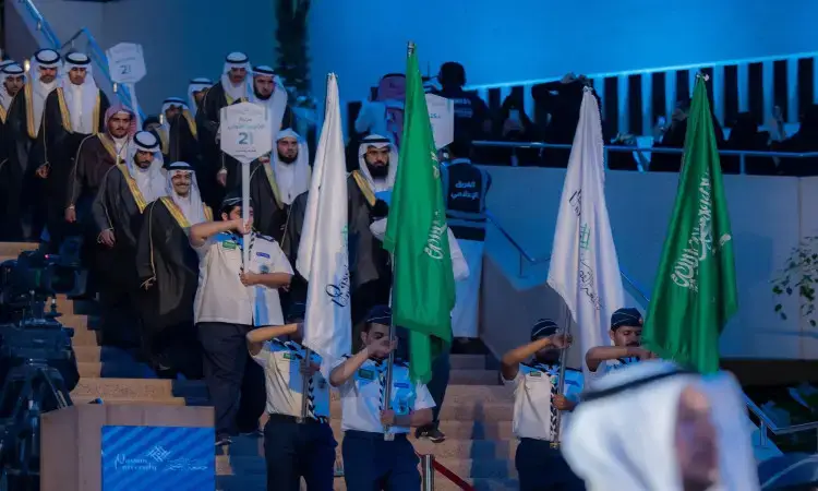 في تخريج في القصيم، تقدم مجموعة من الرجال مرتدين الغتر والشماق السعودية مع العقال والبشت السعودي، يسيرون نزولاً من الدرج خلف كشافة الأعلام الخضراء والبيضاء. يضفي الإضاءة الزرقاء إلى أقصى اليمين، أثناء ضبط العمل لملاحظة تحمل أرقاماً وعبارات للأطفال باللغة العربية. ويتقدم الموكب صاحب السمو أمير منطقة القصيم.
