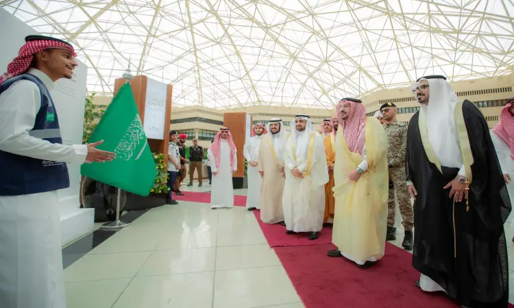 يسير مجموعة من الرجال مرتدين الغترة أو الشماغ السعودي مع العقال، وقد اكتسى الشركاء البشت السعودي، يأمرهم منطقة القصيم، على السجادة الحمراء داخل مبنى حديث ذي سقف الزجاجي. عصر أحد العلم السعودي خلال فترة استقبالهم لبعضهم لفترة مؤقتة فيصل بن مشعل لحفظ القرآن الكريم التي تقام في جامعة القصيم.