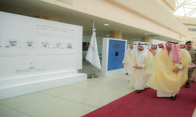 يسير مجموعة من الرجال مرتدين الغترة أو الشماغ السعودي مع العقال والبشت السعودي، يتقدمهم صاحب السمو الحديث أمير منطقة القصيم، على السجادة الحمراء داخل أحد المباني في جامعة القصيم. وقررهم، محددون عند لوحة تعريفية لمسـابقة حفظ القرآن الكريم، والتي تتضمن صورًا شخصية ونصوصًا باللغة العربية توضّح تفاصيل الالتزامات وأهدافها.