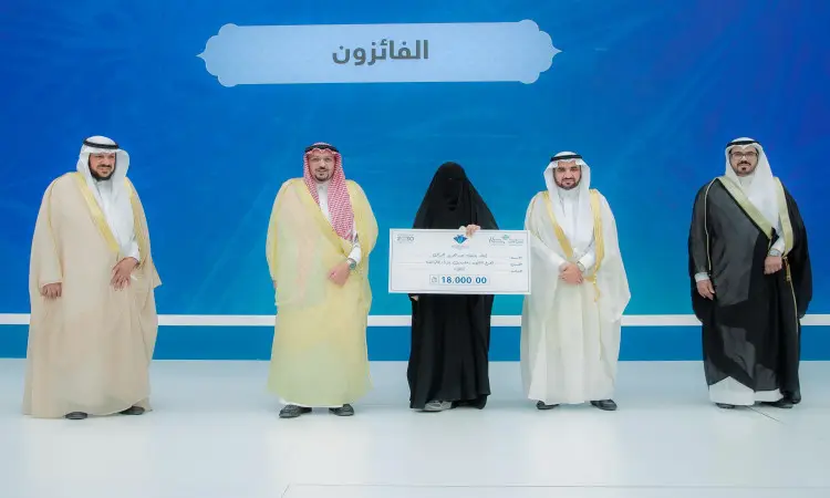 يجتمع خمسة أشخاص على منصة خضراء ضمن فعاليات مسابقة حفظ القرآن الكريم في جامعة القصيم. وسط المجموعة ترتدي عباية سوداء وتحمل شيكًا بشكل معقول، بينما لمسة السيدة بجانبها عدد من الرجال تتحمل الشماغ السعودي والعقال والبشت السعودي، تحت كوفيد "الفائزون" بالجامعة، حيث تم تكريمهم من قبل أمير منطقة القصيم.